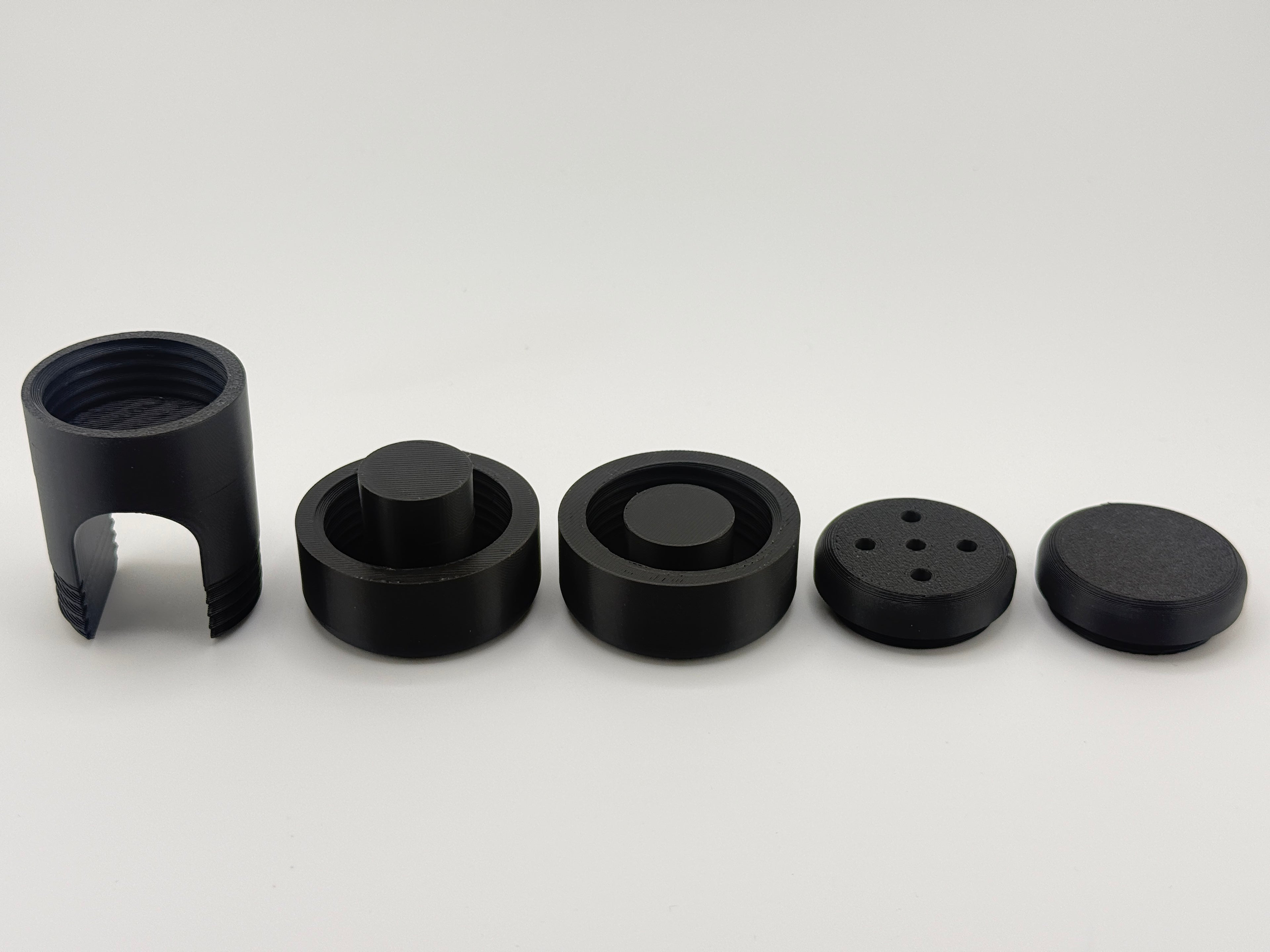 All five black TrackMount parts in a row: main body, two clamping caps, perforated cap, and solid cap