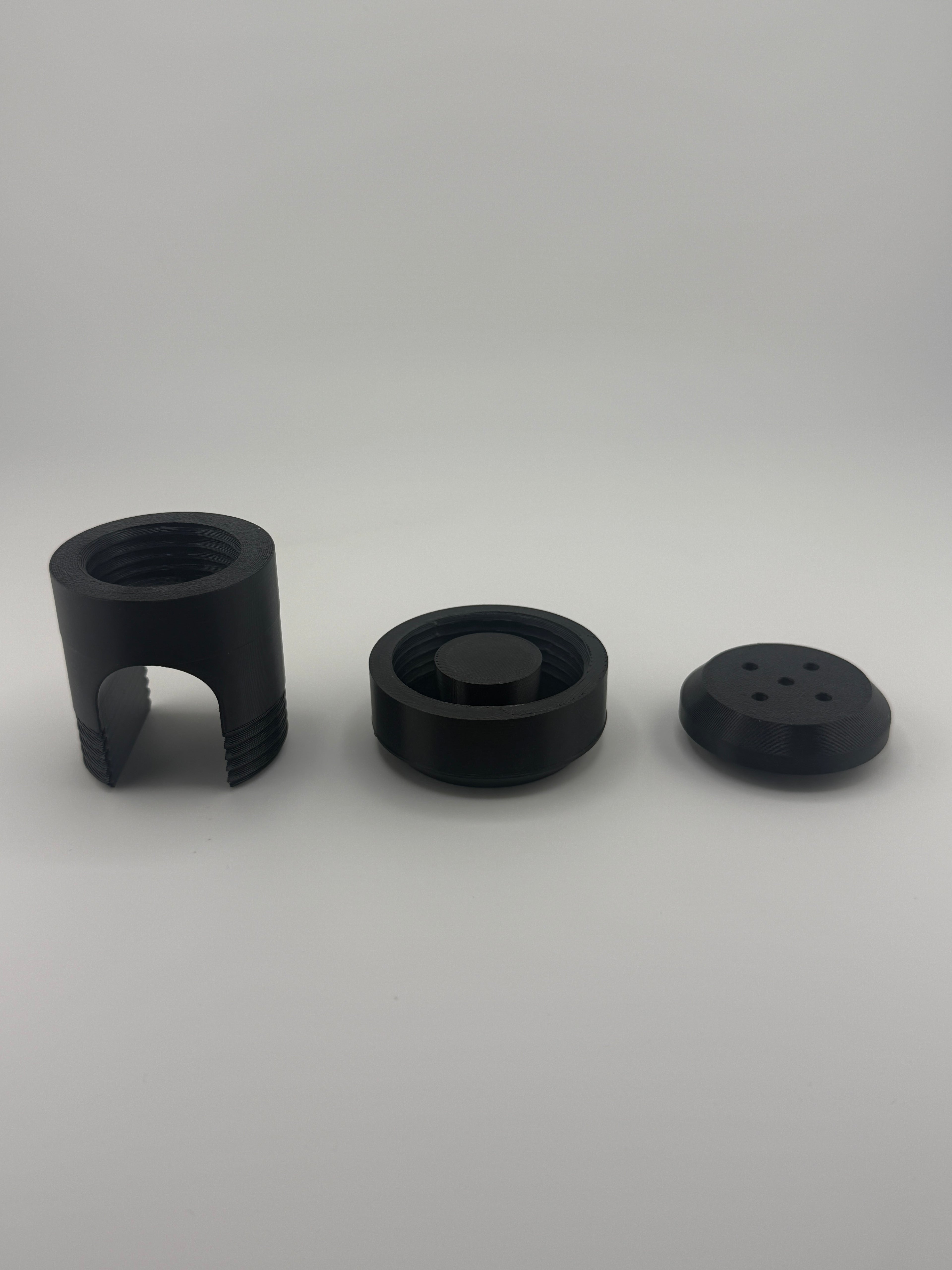 TrackMount XL three-part kit laid out: main body, main cap, and perforated cap in black PETG